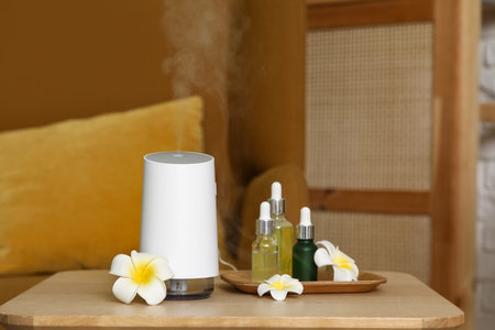 Air humidifier with essential oils and plumeria flowers on table in room