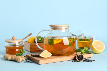 Glass teapot of tasty fruit tea and ingredients on blue backgroundの写真素材