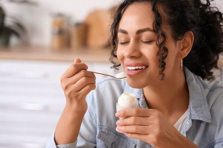 Young African-American woman eating boiled egg in kitchen, closeupの写真素材