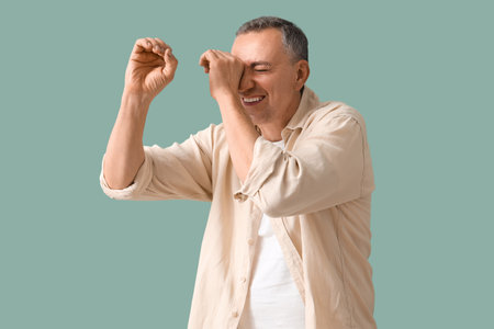 Mature man looking through imaginary spyglass on green backgroundの写真素材