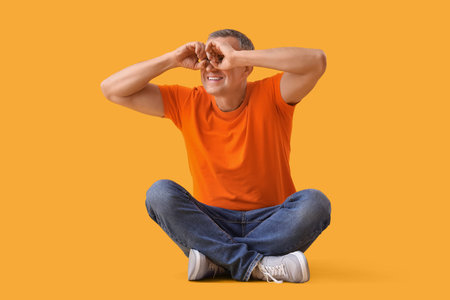 Mature man looking through imaginary binoculars on yellow background