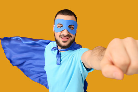 Young man dressed as superhero on orange backgroundの写真素材