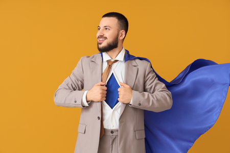 Young businessman in superhero costume under his suit on orange backgroundの写真素材