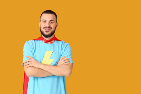 Young man dressed as superhero on orange backgroundの写真素材