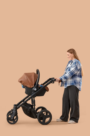 Young mother with her little baby in stroller on beige background