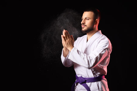 Young man with purple belt practicing karate on black background