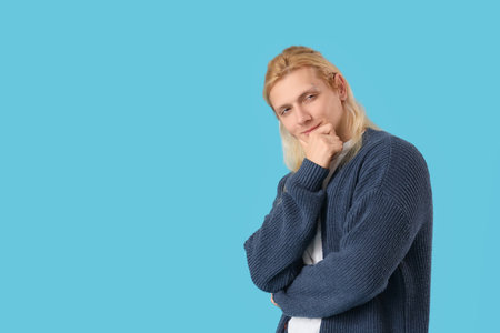 Thoughtful young blonde man in cardigan on blue backgroundの写真素材