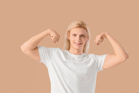 Young blonde man in white t-shirt showing muscles on beige backgroundの写真素材