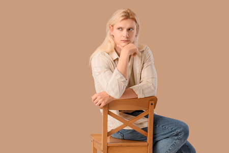 Thoughtful young blonde man in chair on beige backgroundの写真素材
