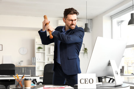 Angry businessman with bat at table in officeの写真素材