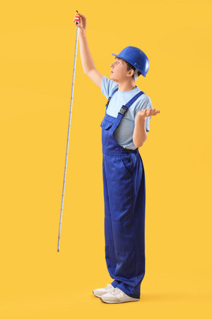 Young male construction worker measuring something with tape on yellow backgroundの写真素材