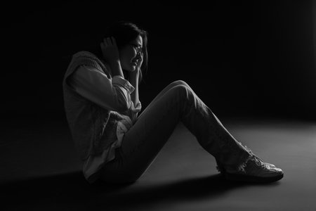 Scared young woman sitting on black backgroundの写真素材