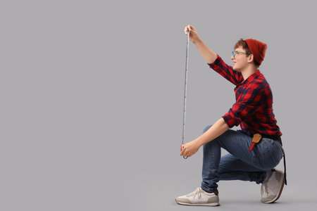 Young man measuring something with tape on gray background