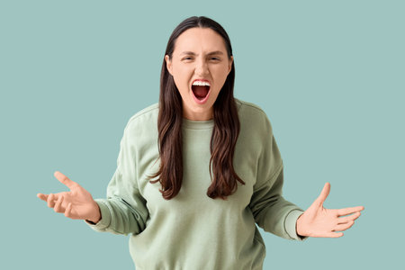 Angry young woman screaming on green background