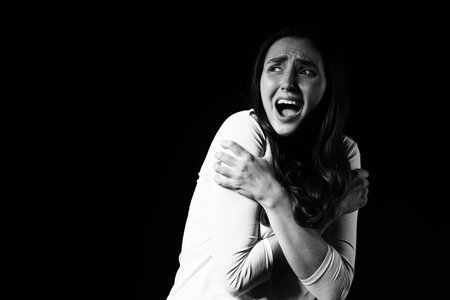 Scared young woman screaming on dark backgroundの写真素材