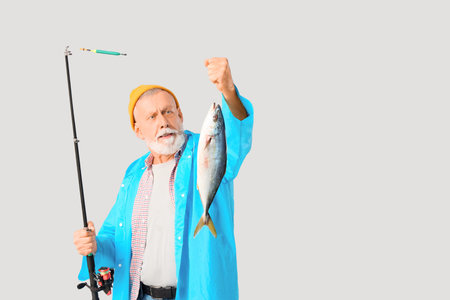 Senior man with fishing rod and caught fish on light background