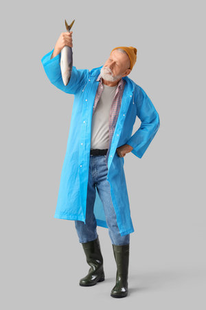 Senior fisherman with fish on light backgroundの写真素材