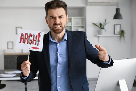 Angry businessman with paper sign pointing at viewer in officeの写真素材