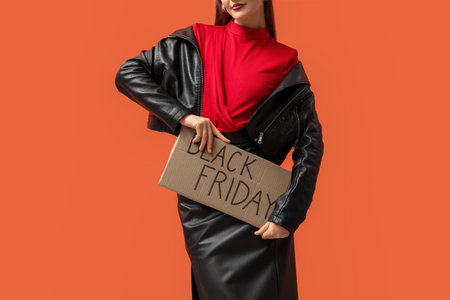 Young woman holding poster with text BLACK FRIDAY on orange backgroundの写真素材