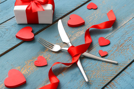 Table setting for Valentine's Day with cutlery, decorative hearts, ribbon and gift box on wooden backgroundの写真素材
