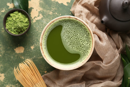 Bowl of fresh matcha tea with powder, chasen and teapot on green grunge background