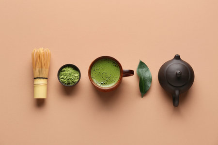 Cup of fresh matcha tea with powder, chasen, leaf and teapot on beige backgroundの写真素材