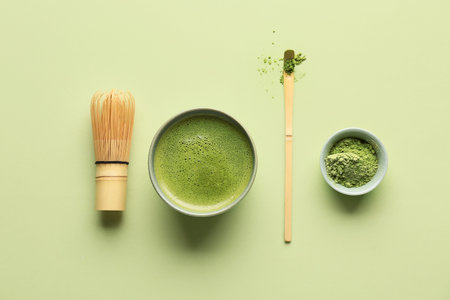 Bowl of fresh matcha tea with powder, chasen and chashaku on green background