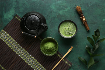 Bowl of fresh matcha tea with powder, chasen, chashaku and teapot on green grunge background