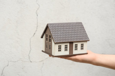 Female hand with house model against cracked wall. Earthquake conceptの写真素材