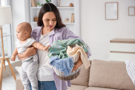Young mother with her baby and laundry basket suffering from postnatal depression at homeの写真素材