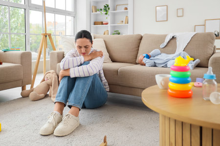 Young mother suffering from postnatal depression and her baby on sofa at homeの写真素材