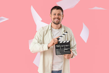 Male actor with movie clapper and falling film script on pink background