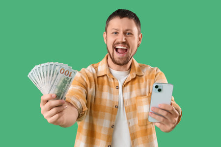 Happy young man with money and mobile phone on green background. Sports bet concept