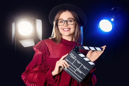 Young actress with movie clapper on dark stageの写真素材
