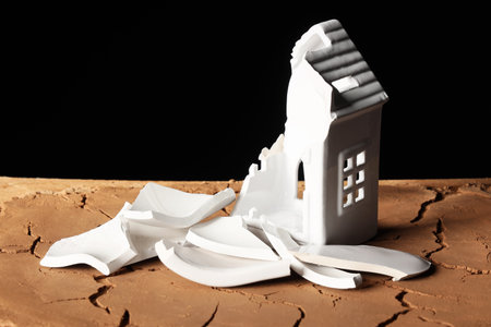 Broken house figure on cracked surface against black background. Earthquake conceptの写真素材