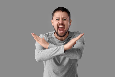 Screaming young man rejecting something on gray background