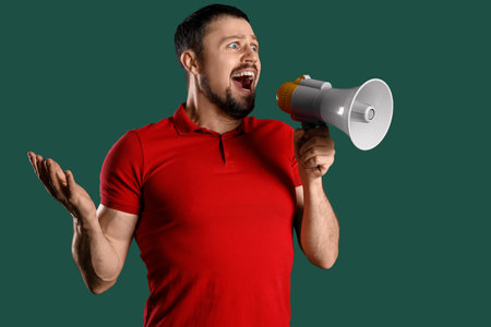 Young man shouting into megaphone on green backgroundの写真素材