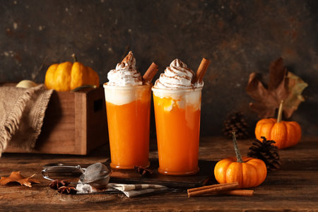 Glasses of orange pumpkin spice latte and ingredients on wooden tableの写真素材
