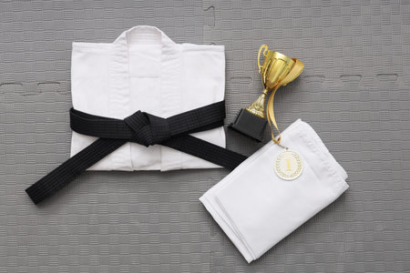 Karate uniform with black belt and gold cup on gray mat