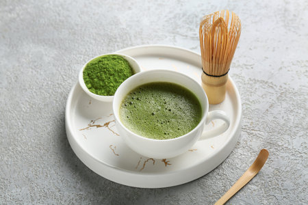 Tray with cup of matcha tea and chasen on gray grunge background, closeup