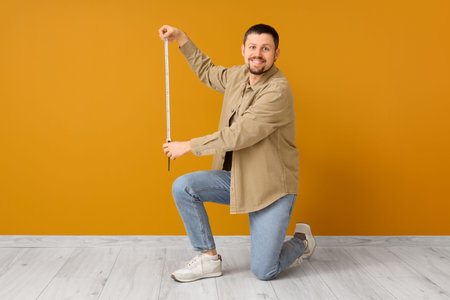 Young man with tape measure near orange wall