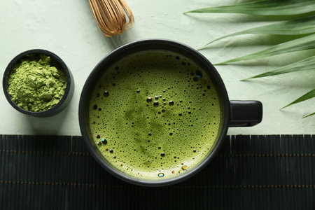 Composition with wicker mat, bowl of tasty matcha tea and tropical leaf on green grunge background,...