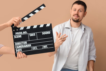 Male actor and female hands with movie clapper on beige backgroundの写真素材