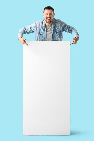 Young man pointing at blank poster on blue backgroundの写真素材