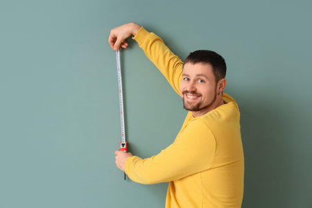 Young man with tape measure on green background