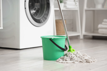 Mop with green bucket of water on floor in bathroomの写真素材