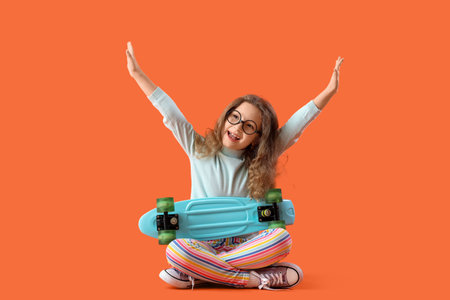 Cute little girl with skateboard sitting on orange backgroundの写真素材