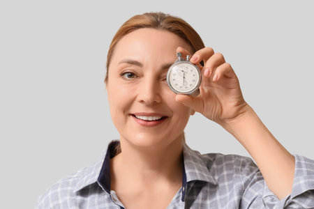 Mature woman with stopwatch on light background, closeup