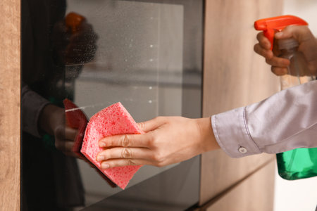 Female hands with sponge cleaning oven in kitchen, closeupの写真素材