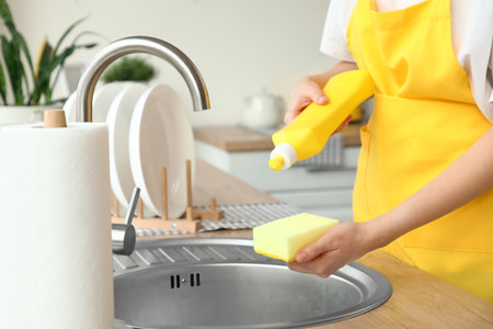 Female janitor pouring dish soap on cleaning sponge in kitchenの写真素材